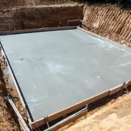 Wylany fundament pod budynek w wykopie, z widocznym deskowaniem i poziomowaniem, przygotowany do dalszych prac budowlanych.