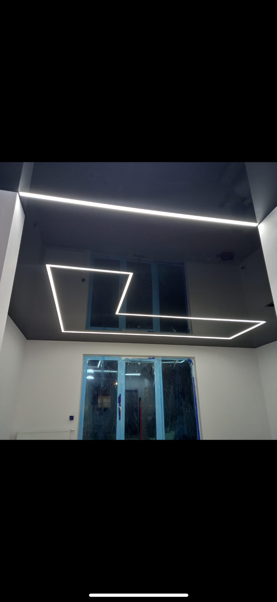 Nowoczesne oświetlenie LED na czarnym, lustrzanym suficie w jasnym pomieszczeniu, okna zabezpieczone folią ochronną.