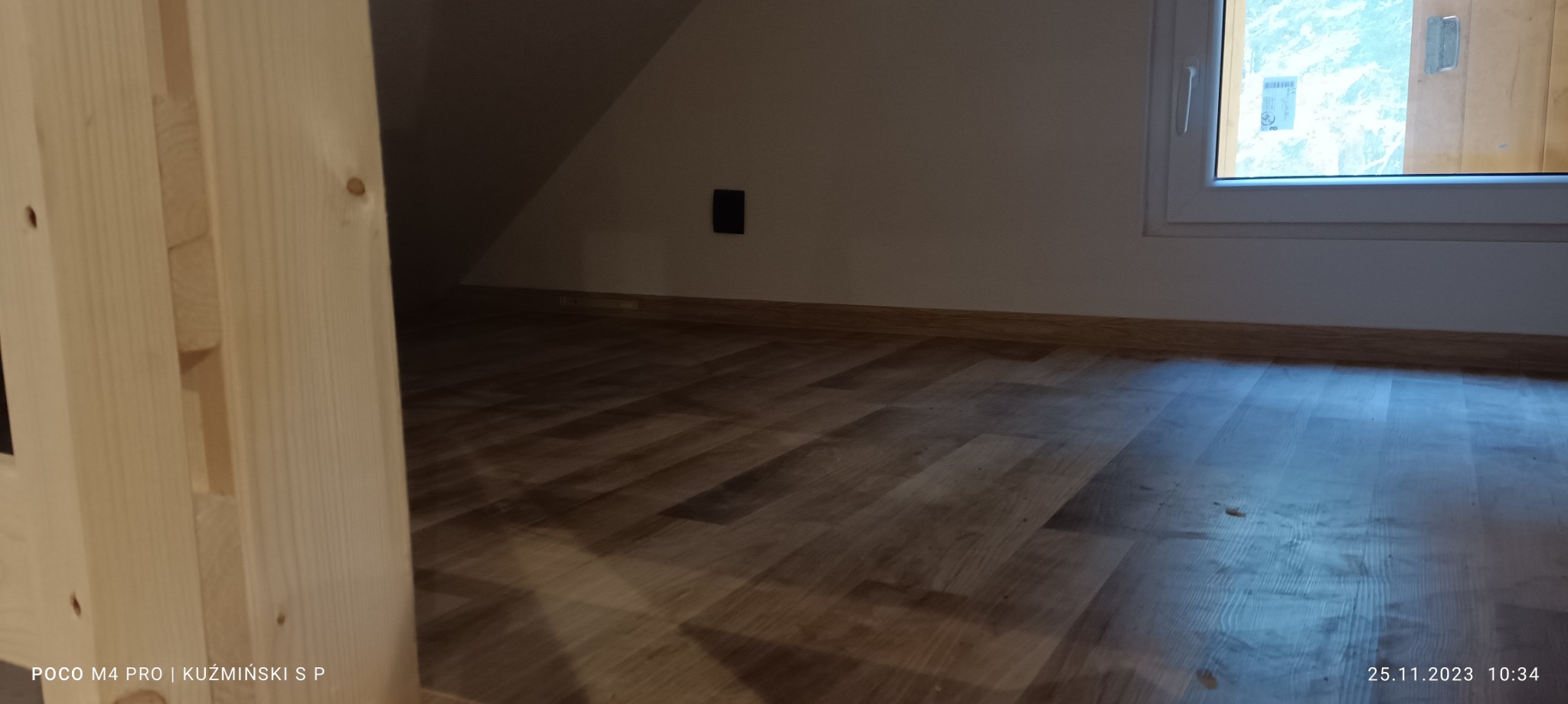 Nowo ułożone panele podłogowe w pokoju na poddaszu, widoczne listwy przypodłogowe i fragment drewnianej konstrukcji po lewej stronie.