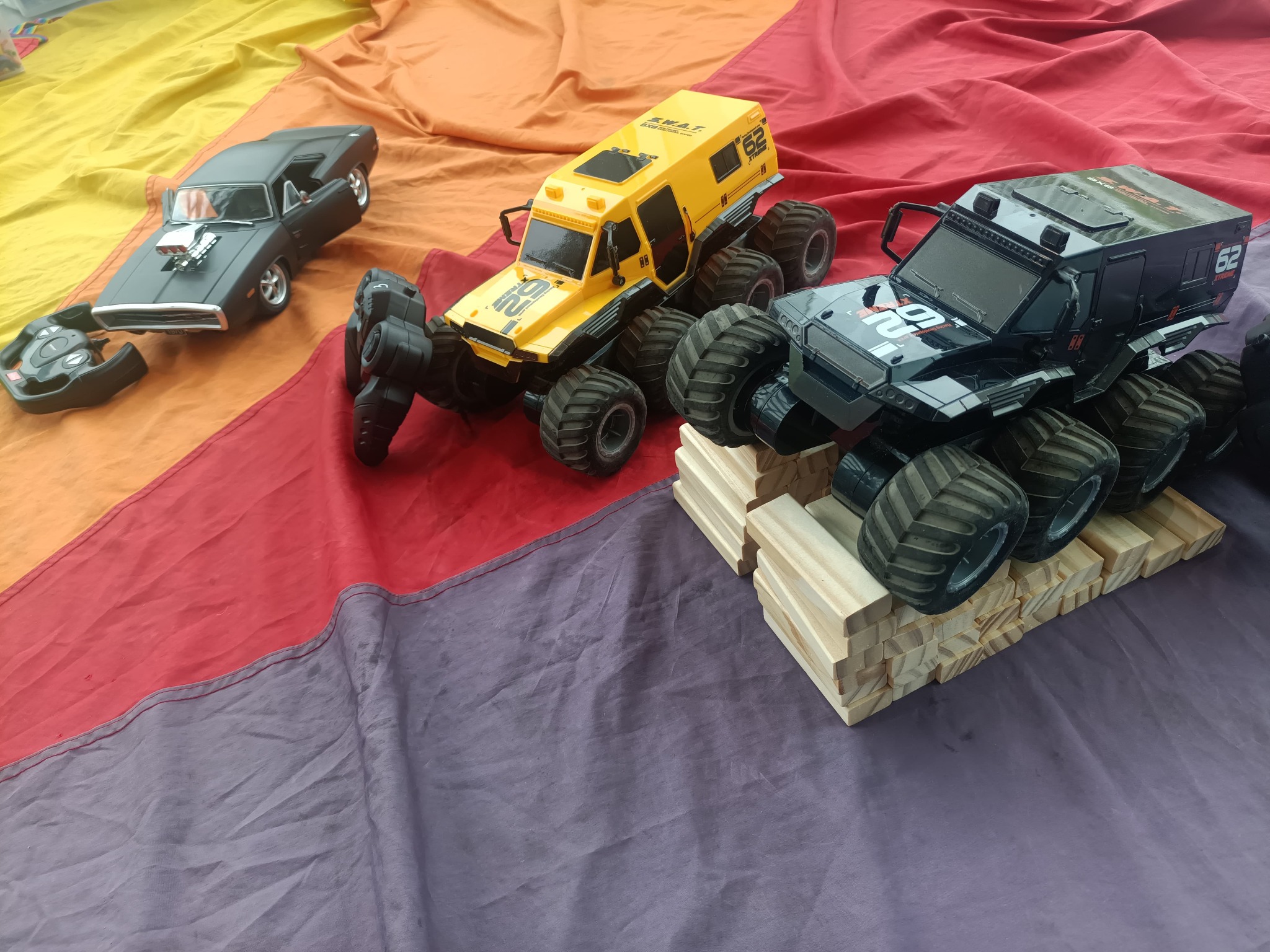 Trzy zdalnie sterowane pojazdy (muscle car i dwa monster trucki z numerem 62) na kolorowym tle. Zabawki dla dzieci na imprezę tematyczną.