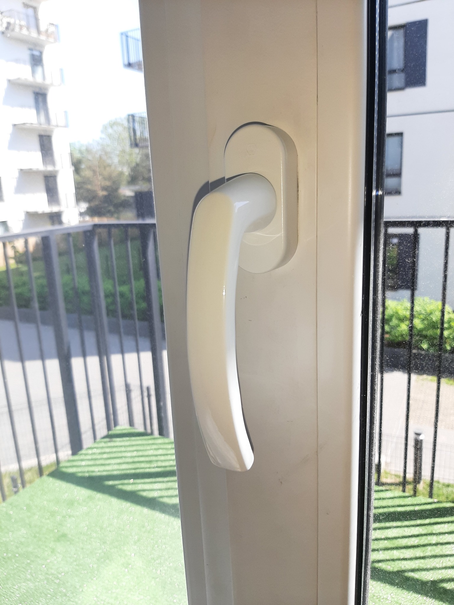 Zamknięte białe okno PCV z widokiem na balkon i budynek mieszkalny w Zgierzu.