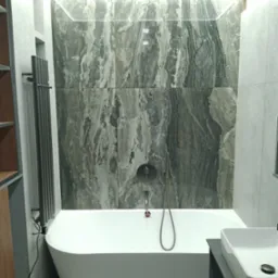 Nowoczesna łazienka z białą wanną wolnostojącą, marmurowe płytki na ścianie podświetlone ledami, grzejnik drabinkowy i umywalka nablatowa.