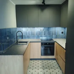 Nowoczesna kuchnia w odcieniach szarości i beżu z niebieskimi płytkami na ścianie, czarną armaturą i wzorzystą podłogą.