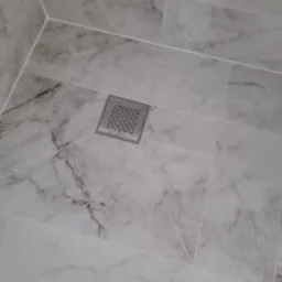 Posadzka łazienkowa wyłożona marmurowymi płytkami z centralnie umieszczonym, kwadratowym odpływem liniowym ze stali nierdzewnej.