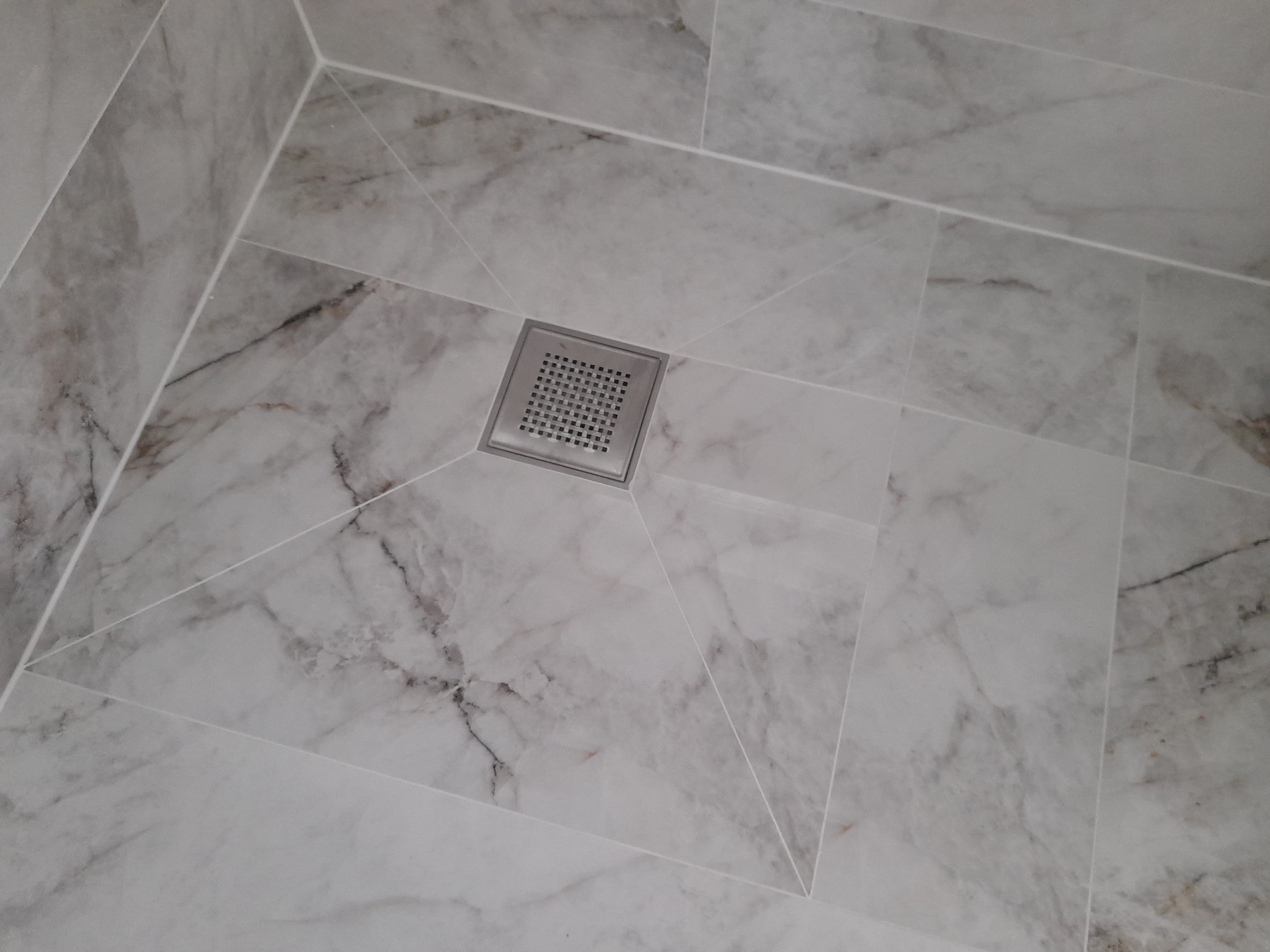 Posadzka łazienkowa wyłożona marmurowymi płytkami z centralnie umieszczonym, kwadratowym odpływem liniowym ze stali nierdzewnej.