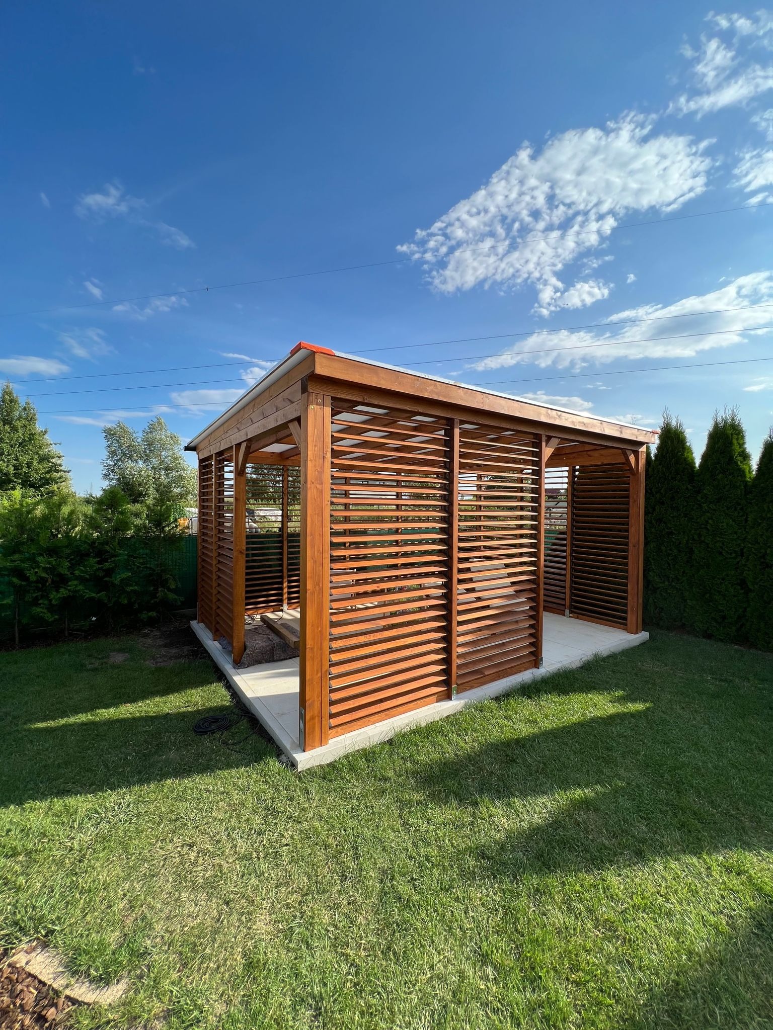 Pergola drewniana pokryta poliwęglanem komorowym, obudowana ruchomymi deseczkami.