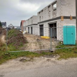 ADNN Adam Płecha - Surowe domy murowane z betonu komórkowego w trakcie budowy, widoczne tymczasowe ogrodzenie budowy i toaleta przenośna