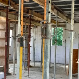 ADNN Adam Płecha - Wnętrze budowy domu w trakcie wznoszenia ścian z betonu komórkowego, widoczne podpory stropowe, szalunki i paleta bloczków Ytong.