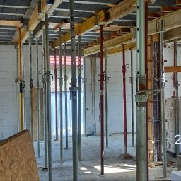 ADNN Adam Płecha - Wnętrze budowy domu w trakcie murowania ścian z betonu komórkowego, widoczne podpory stropowe, szalunki i pustaki.