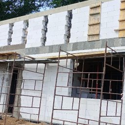 ADNN Adam Płecha - Budowa domu: wznoszenie ścian z białych bloczków, widoczne rusztowania i elementy szalunkowe.