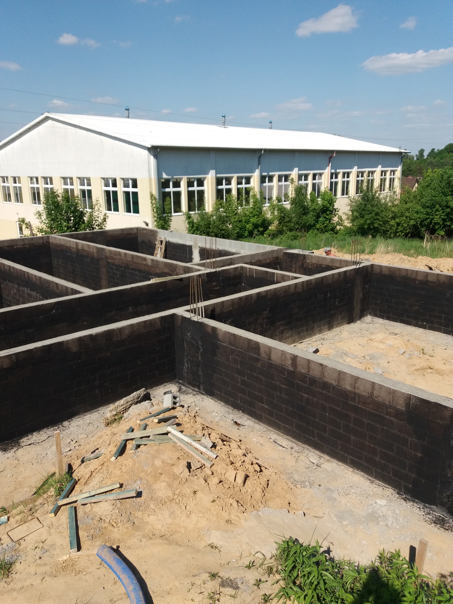 Wrocław: Wylane i zaizolowane fundamenty pod budowę domu, widoczne zbrojenia i pozostałości materiałów budowlanych na placu budowy, w tle budynek gospodarczy.