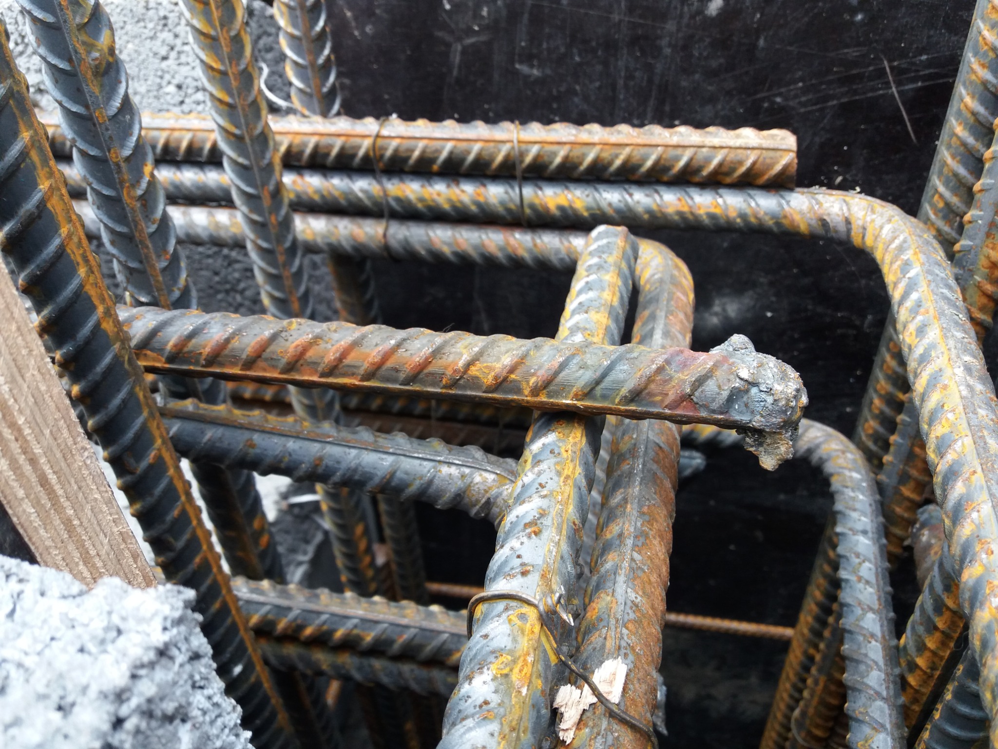 Zbrojenie fundamentowe z prętów żebrowanych, częściowo pokrytych rdzą, ułożone w przestrzenny szkielet z widocznymi elementami drewnianego szalunku i betonu.