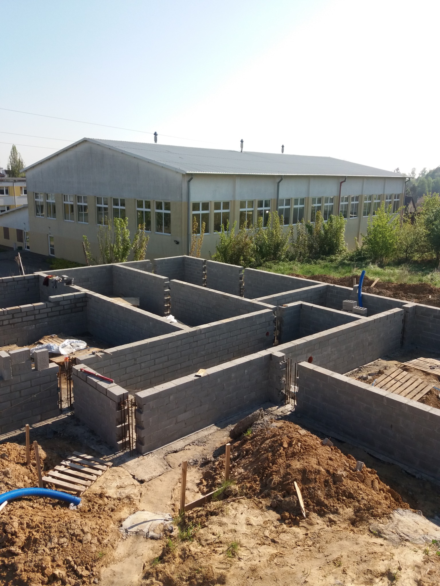 Wzniesione z bloczków fundamenty domu, widoczne zbrojenia, w tle budynek gospodarczy pod błękitnym niebem.