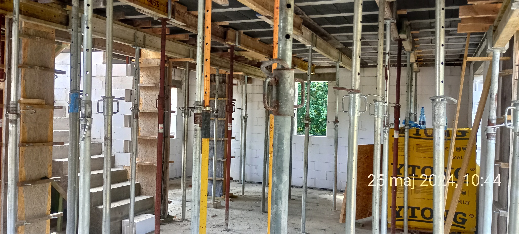 Wnętrze budowy domu w trakcie wznoszenia ścian z betonu komórkowego, widoczne podpory stropowe, szalunki i paleta bloczków Ytong.