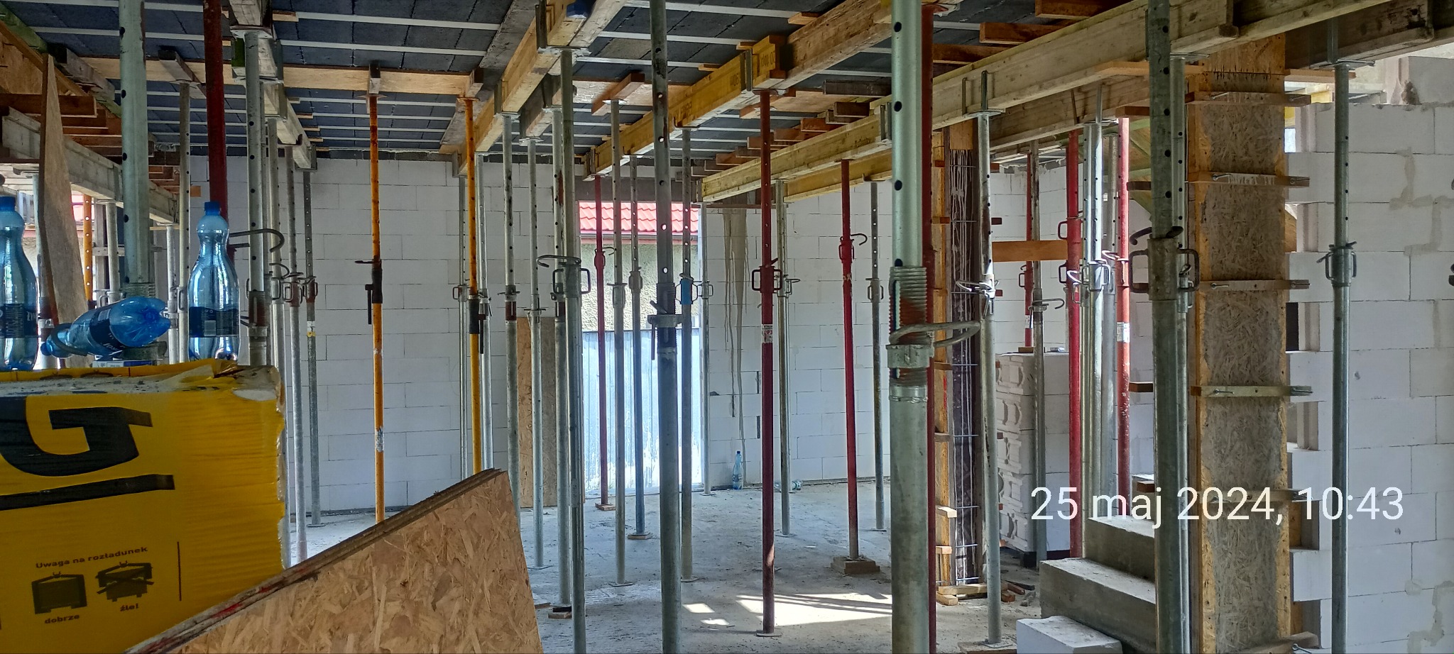 Wnętrze budowy domu w trakcie murowania ścian z betonu komórkowego, widoczne podpory stropowe, szalunki i pustaki.