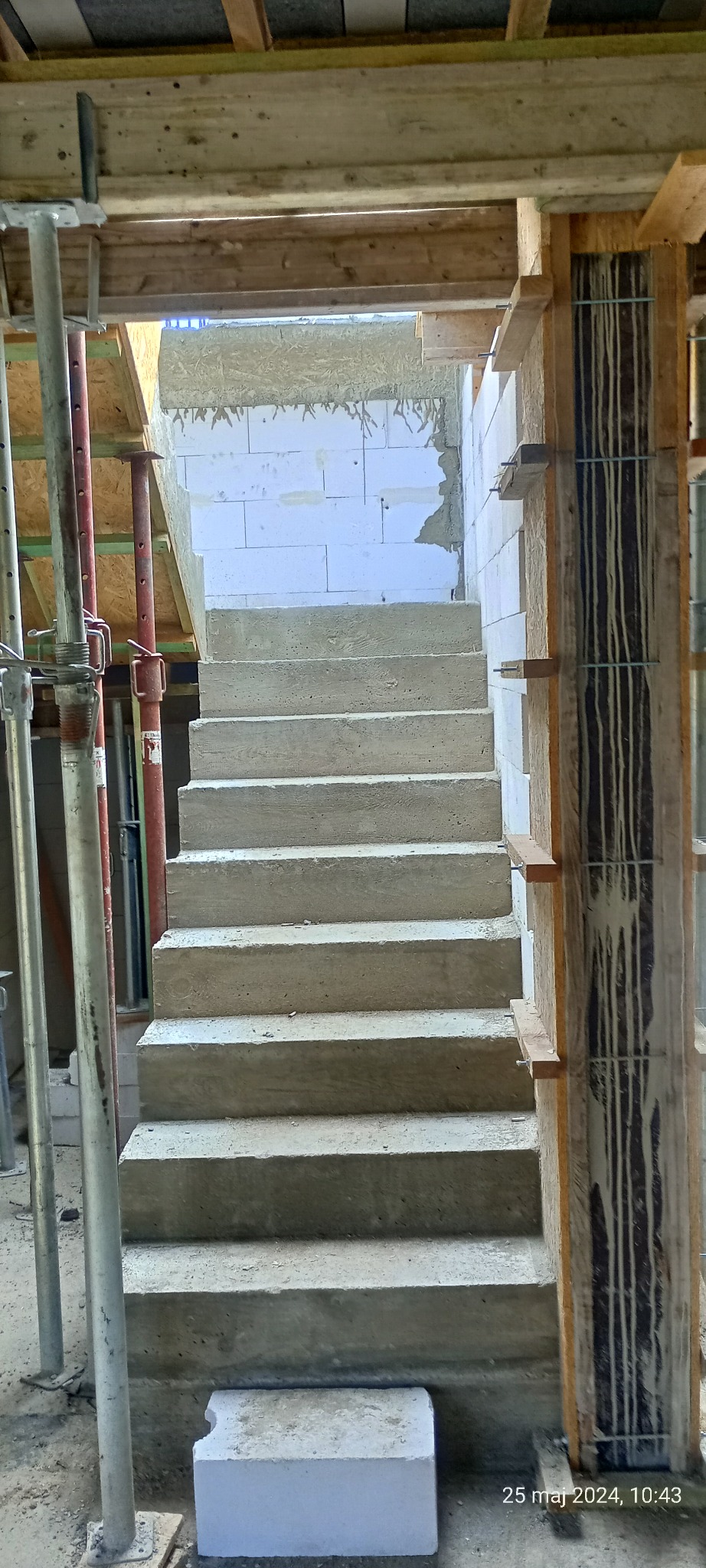 Wewnętrzne betonowe schody w trakcie budowy, widoczne szalunki i podpory, ściany z bloczków białych.