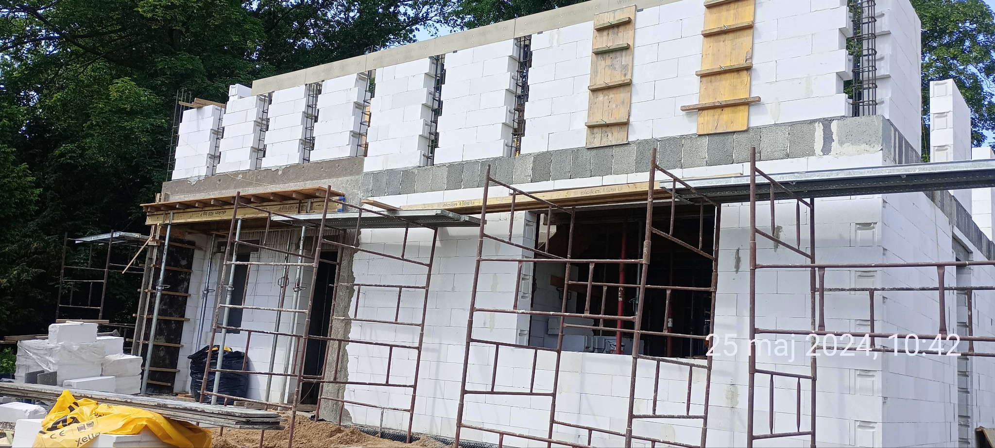 Budowa domu: wznoszenie ścian z białych bloczków, widoczne rusztowania i elementy szalunkowe.