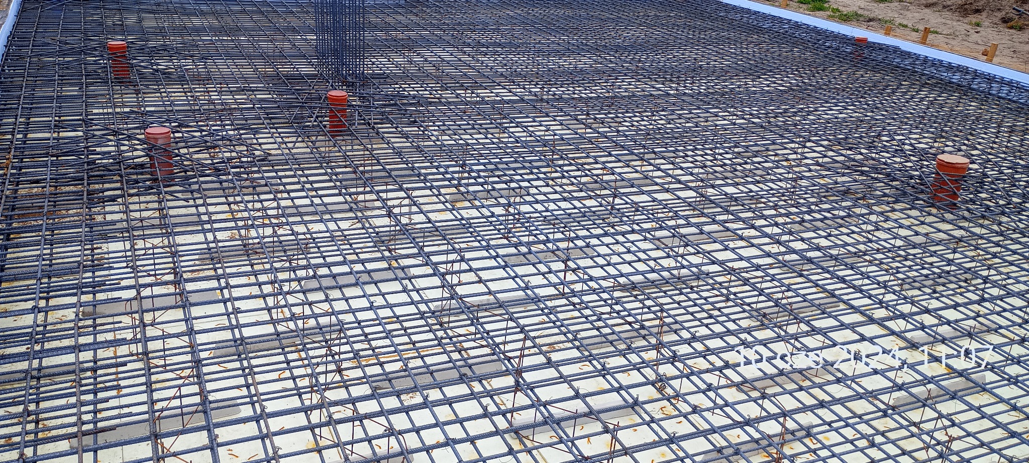 Zbrojenie płyty fundamentowej z widocznymi rurami kanalizacyjnymi i podkładkami dystansowymi.