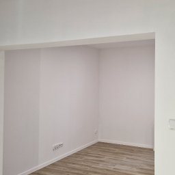 Mar-Greg - Pomalowane na biało wnętrze z drewnopodobną podłogą, widoczne gniazdka i włącznik światła, przygotowane do dalszego wykończenia lub aranżacji.