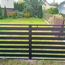 Artur Trawiński - Nowoczesna, czarna, metalowa brama dwuskrzydłowa z poziomymi panelami na tle zielonego trawnika i ogrodu.