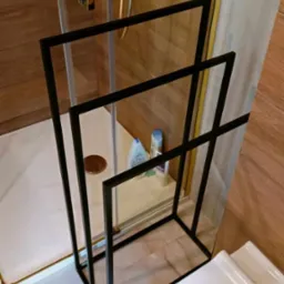 Czarny, metalowy stojak na ręczniki w łazience z kabiną prysznicową i drewnopodobnymi płytkami na ścianach.