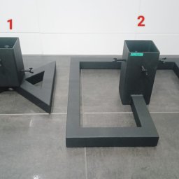 Artur Trawiński - Dwie metalowe podstawy, pomalowane proszkowo na czarno, wykonane w Kole. Jedna w kształcie trójkąta, druga w kształcie prostokąta z kwadratową tuleją, obie z widocznymi śrubami regulacyjnymi.