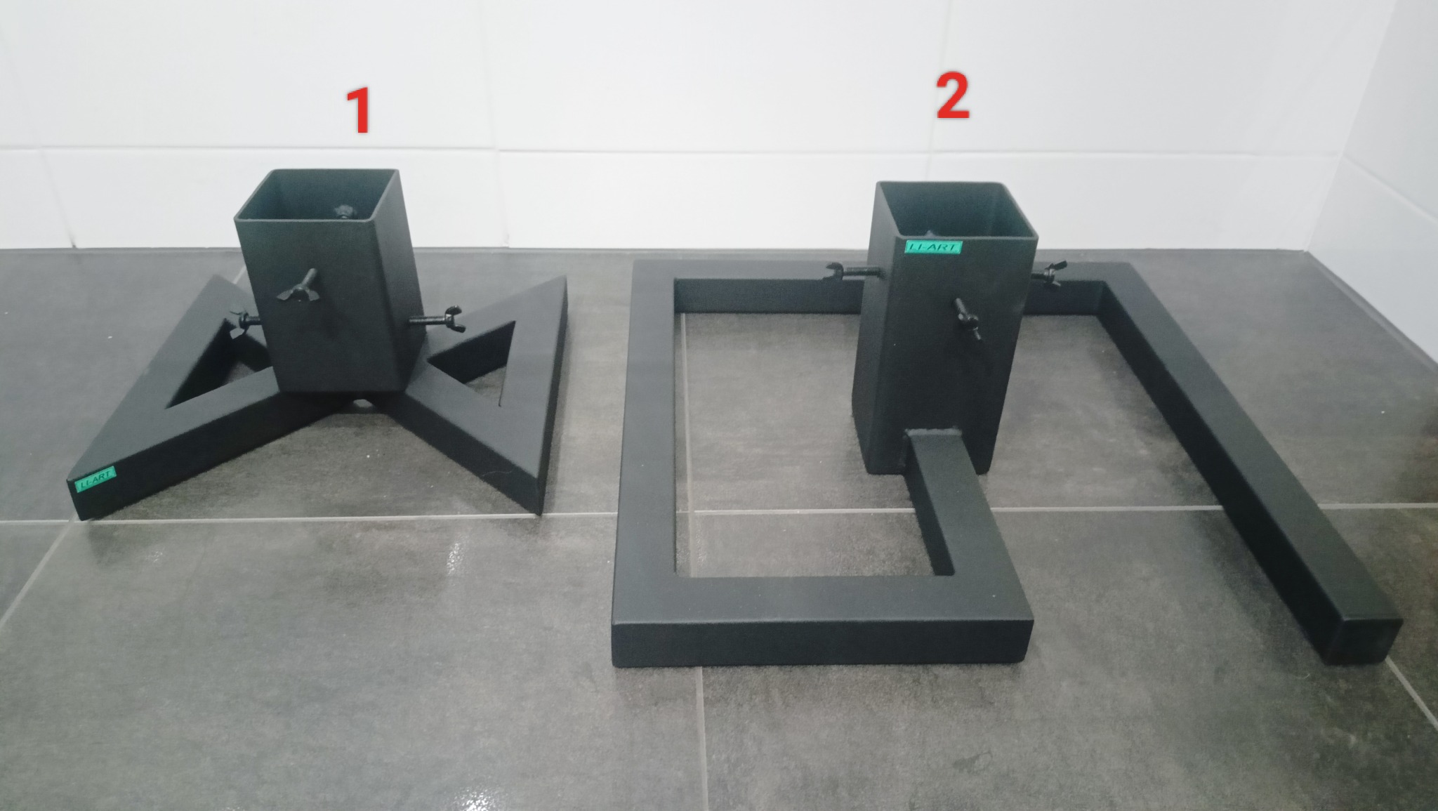 Dwie metalowe podstawy, pomalowane proszkowo na czarno, wykonane w Kole. Jedna w kształcie trójkąta, druga w kształcie prostokąta z kwadratową tuleją, obie z widocznymi śrubami regulacyjnymi.