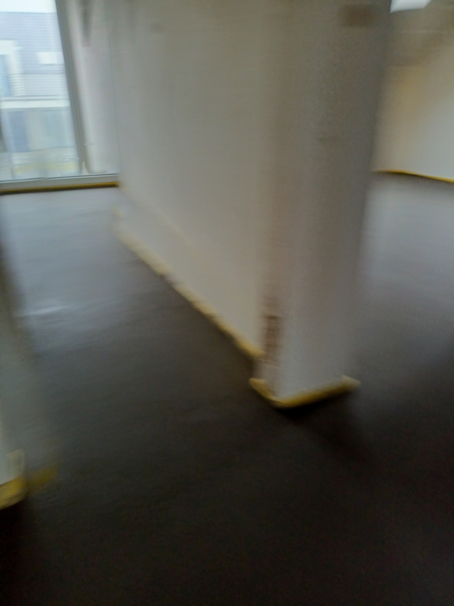 Świeżo wylana, ciemna posadzka jastrychowa, zabezpieczona folią przy ścianach, w jasnym pomieszczeniu z oknem.