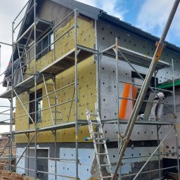 Eugeniusz Harasim - Dom w trakcie prac elewacyjnych: ocieplenie wełną mineralną i styropianem, widoczne rusztowania i pracownicy. Etap pośredni prac, detale montażu.