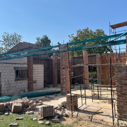 DACH-MAT Mateusz Russu - Rozbiórka i budowa nowej konstrukcji budynku z cegły i pustaków, widoczne rusztowania i pracownicy w trakcie prac, gruz na ziemi.