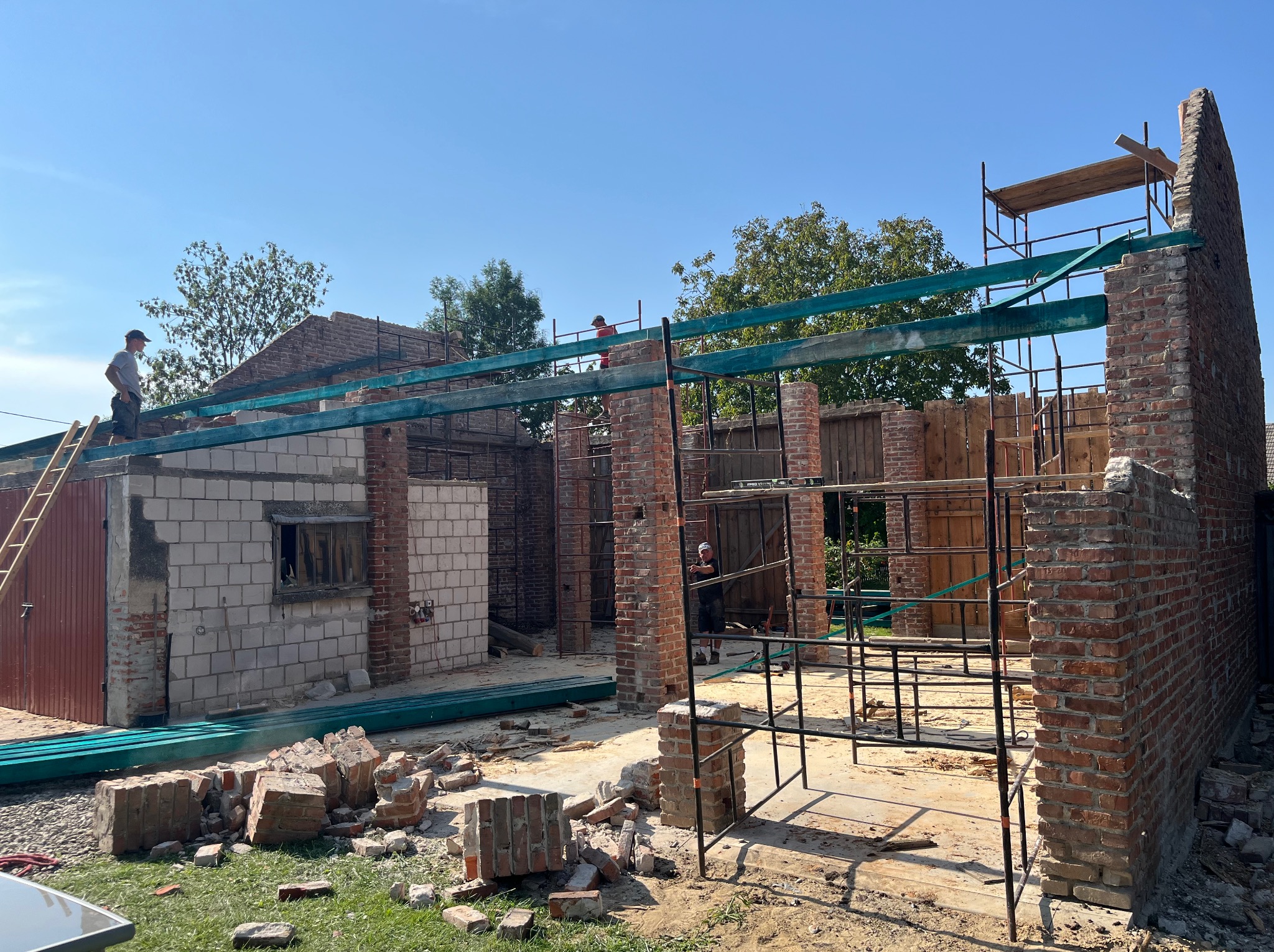 Rozbiórka i budowa nowej konstrukcji budynku z cegły i pustaków, widoczne rusztowania i pracownicy w trakcie prac, gruz na ziemi.