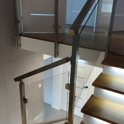 INOXSPEC Damian Mazurkiewicz - Schody drewniane z podświetleniem LED i balustradą ze stali nierdzewnej oraz szkła, widok z góry, nowoczesne wnętrze.