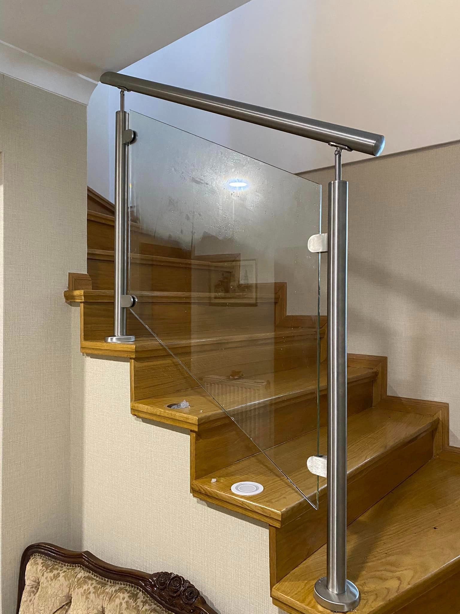 Szklana balustrada ze stalowymi słupkami na drewnianych schodach, widoczne ślady montażu na stopniach.