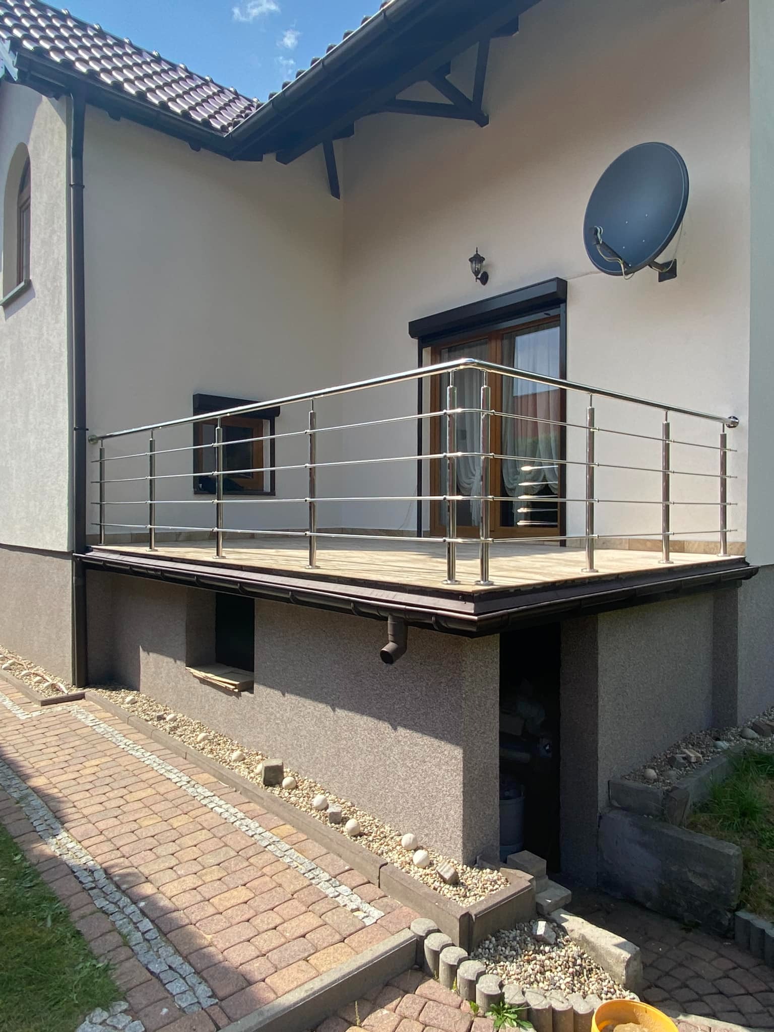 Balkon z balustradą ze stali nierdzewnej, drewnianą podłogą i satelitą na elewacji budynku.