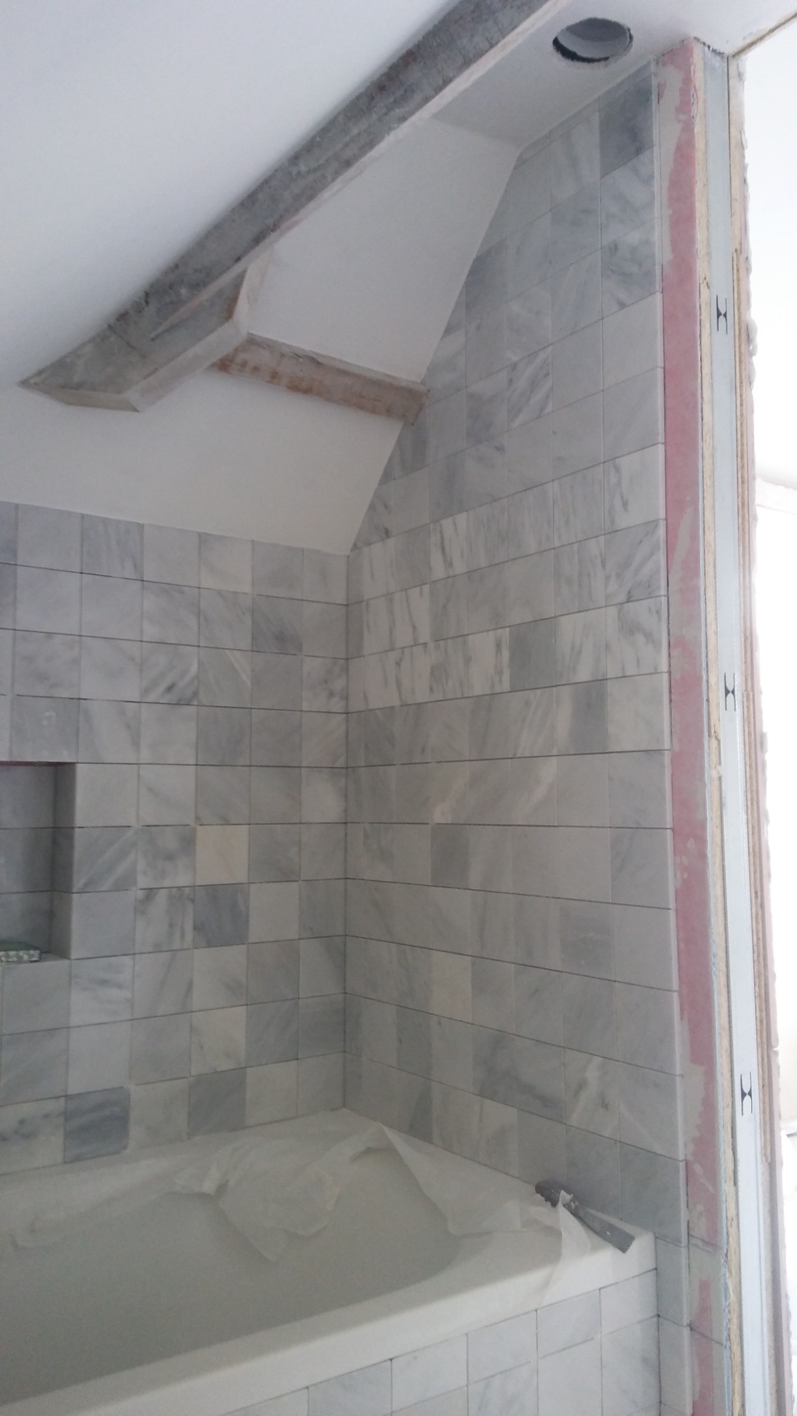 Łazienka w trakcie wykańczania: marmurowe płytki na ścianach, zabezpieczona wanna, widoczne elementy konstrukcyjne sufitu i ościeżnicy.