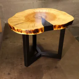 Stolik kawowy z blatem z plastra drewna wypełnionego czarną żywicą epoksydową, osadzony na metalowej, czarnej podstawie w kształcie litery X.