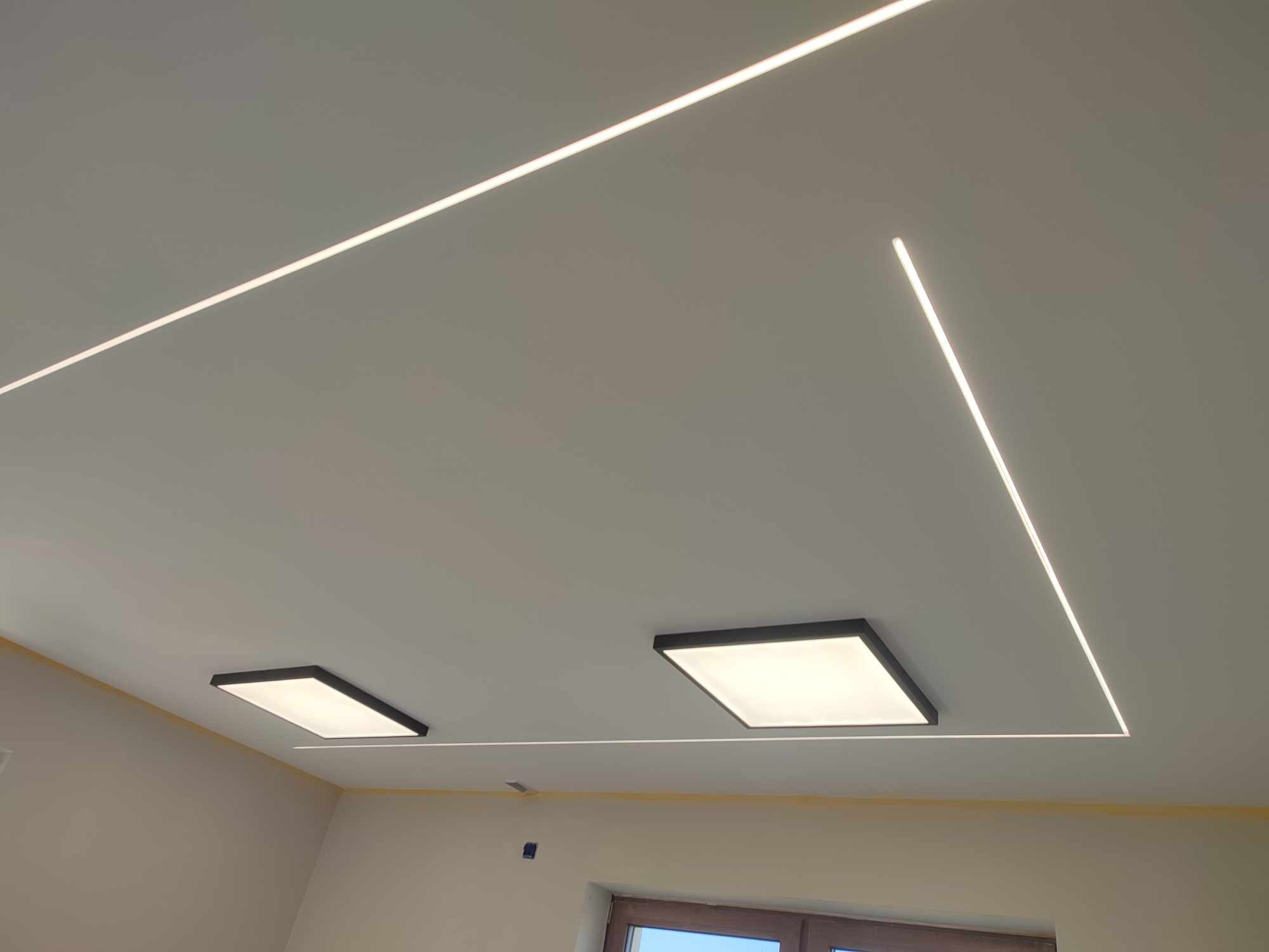 Nowoczesne oświetlenie sufitowe z liniami LED tworzącymi geometryczny wzór, uzupełnione dwoma kwadratowymi panelami LED w czarnych ramkach.