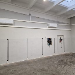 JJN Klimatyzacje Jakub Raubo - Wnętrze pomieszczenia z dwoma zamontowanymi klimatyzatorami ściennymi, widoczne narzędzia na ścianie, betonowa podłoga i białe ściany.