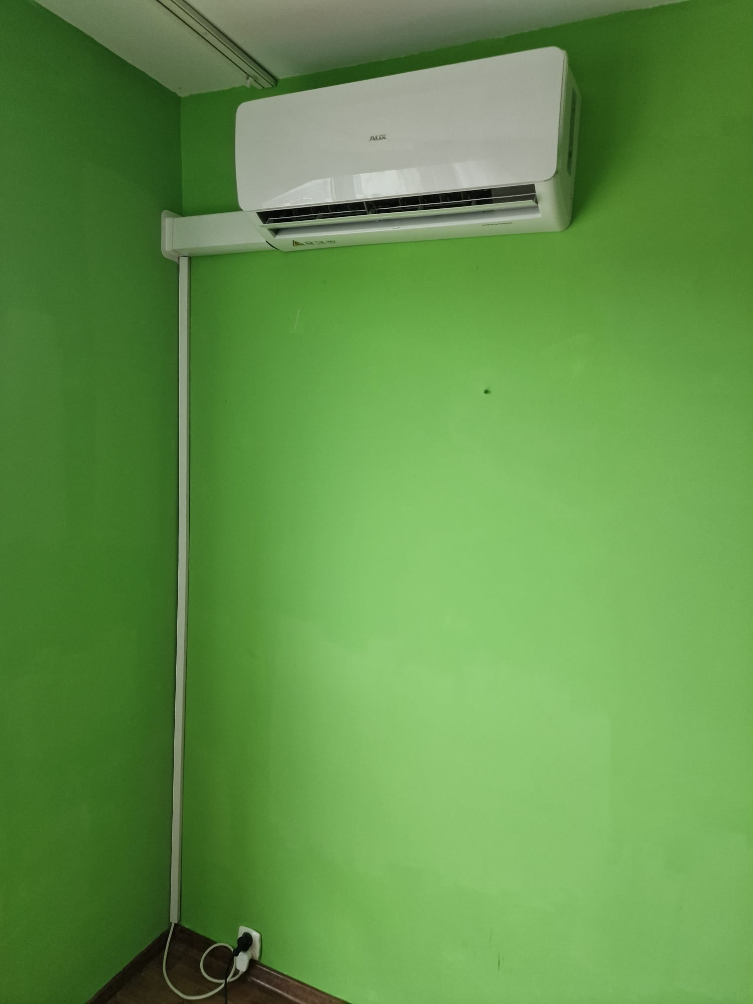 Biały klimatyzator marki AUX zamontowany na jasnozielonej ścianie w pomieszczeniu.