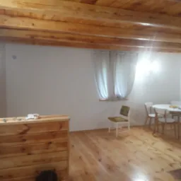 Drewniany sufit z belkami w jasnym pomieszczeniu w Wyszkowie, widoczna drewniana podłoga i fragment stołu z krzesłami.