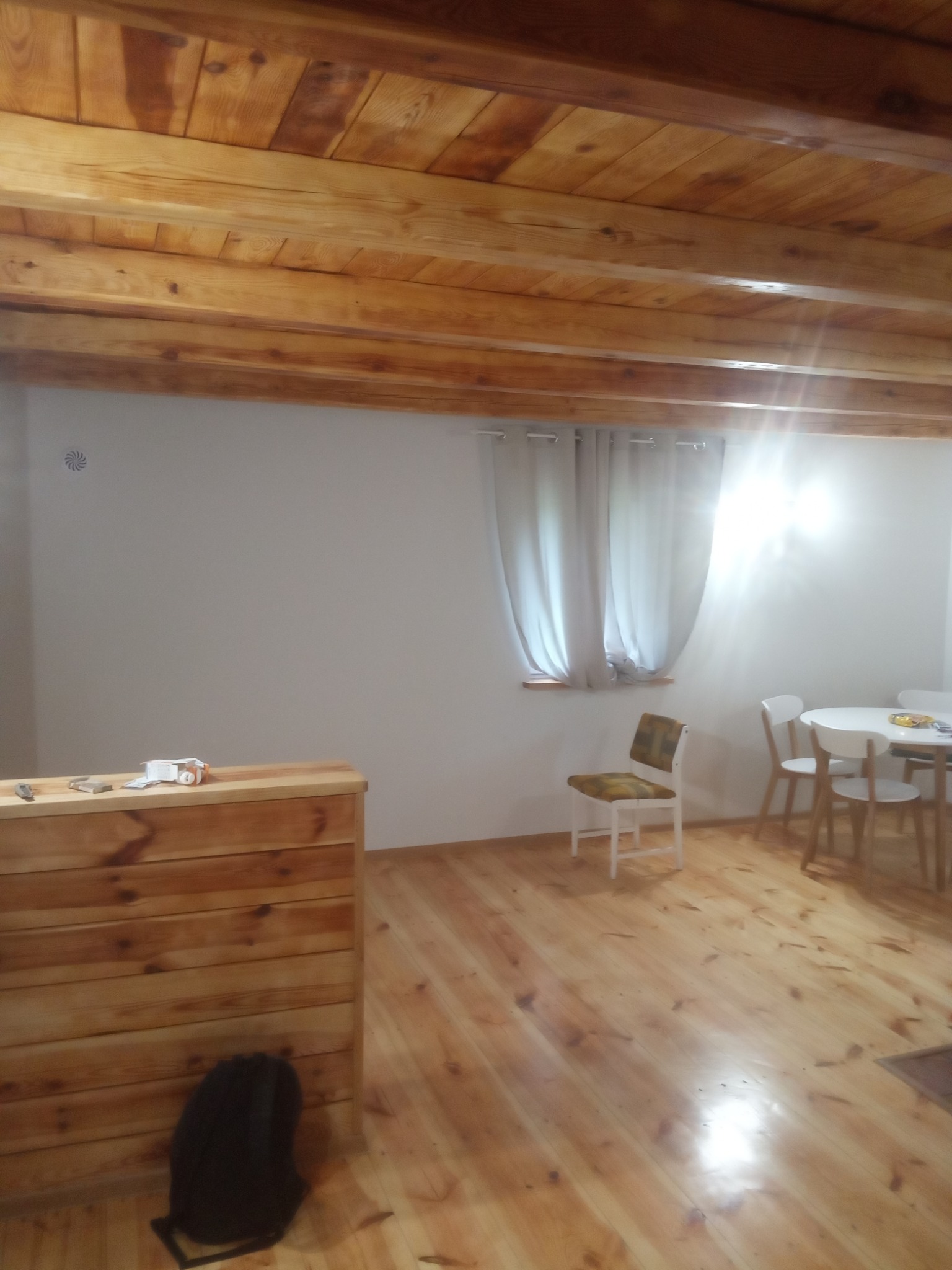 Drewniany sufit z belkami w jasnym pomieszczeniu w Wyszkowie, widoczna drewniana podłoga i fragment stołu z krzesłami.