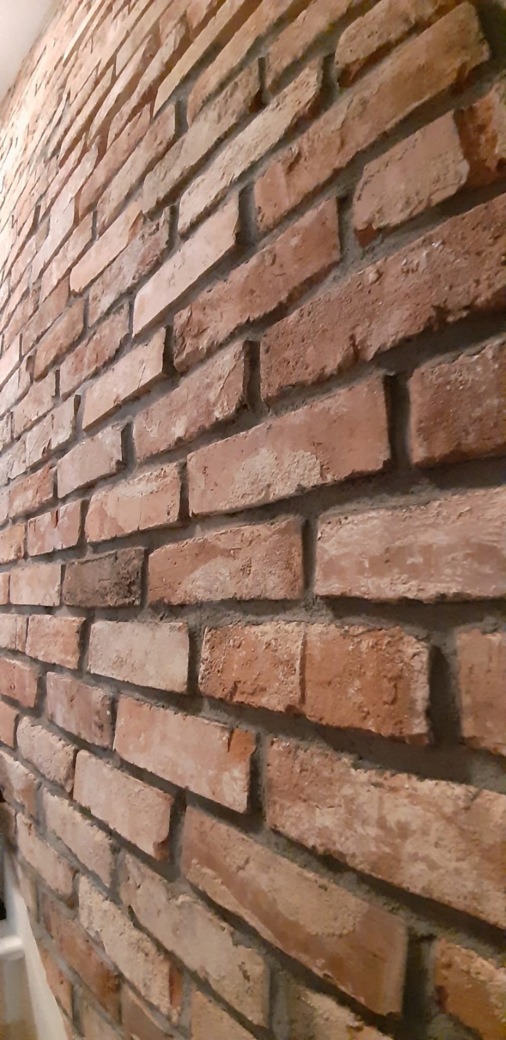 Dekoracyjna ściana z cegły w odcieniach czerwieni i brązu, z wyraźnie widoczną fakturą i fugami, ułożona pod kątem.