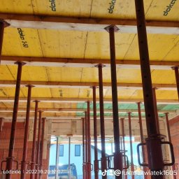 Łukasz Kwiatek - Szczegółowe ujęcie szalunku stropowego Doka 3-S0 z czerwonymi stemplami, widok z dołu na budowie domu z cegły.