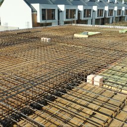 Łukasz Kwiatek - Zbrojenie stropu na budowie domu w Tomaszowie Mazowieckim, widoczne z góry, z ułożonymi bloczkami i deskowaniem. W tle budynki w zabudowie szeregowej.