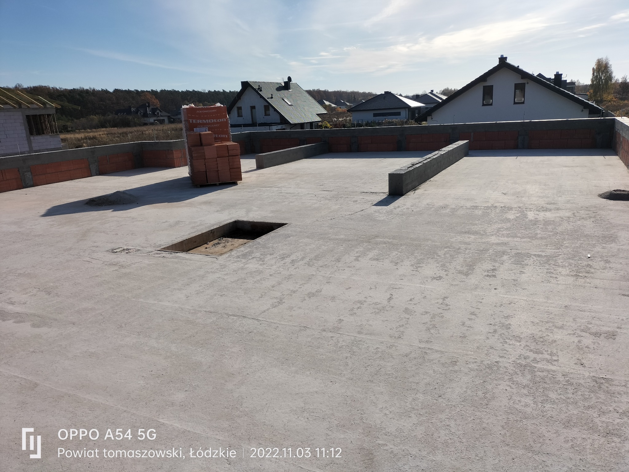 Wylana płyta fundamentowa z wystającymi elementami betonowymi i częściowo wymurowanymi ścianami z bloczków ceramicznych Termoton na obrzeżach. W tle zabudowa jednorodzinna i błękitne niebo.