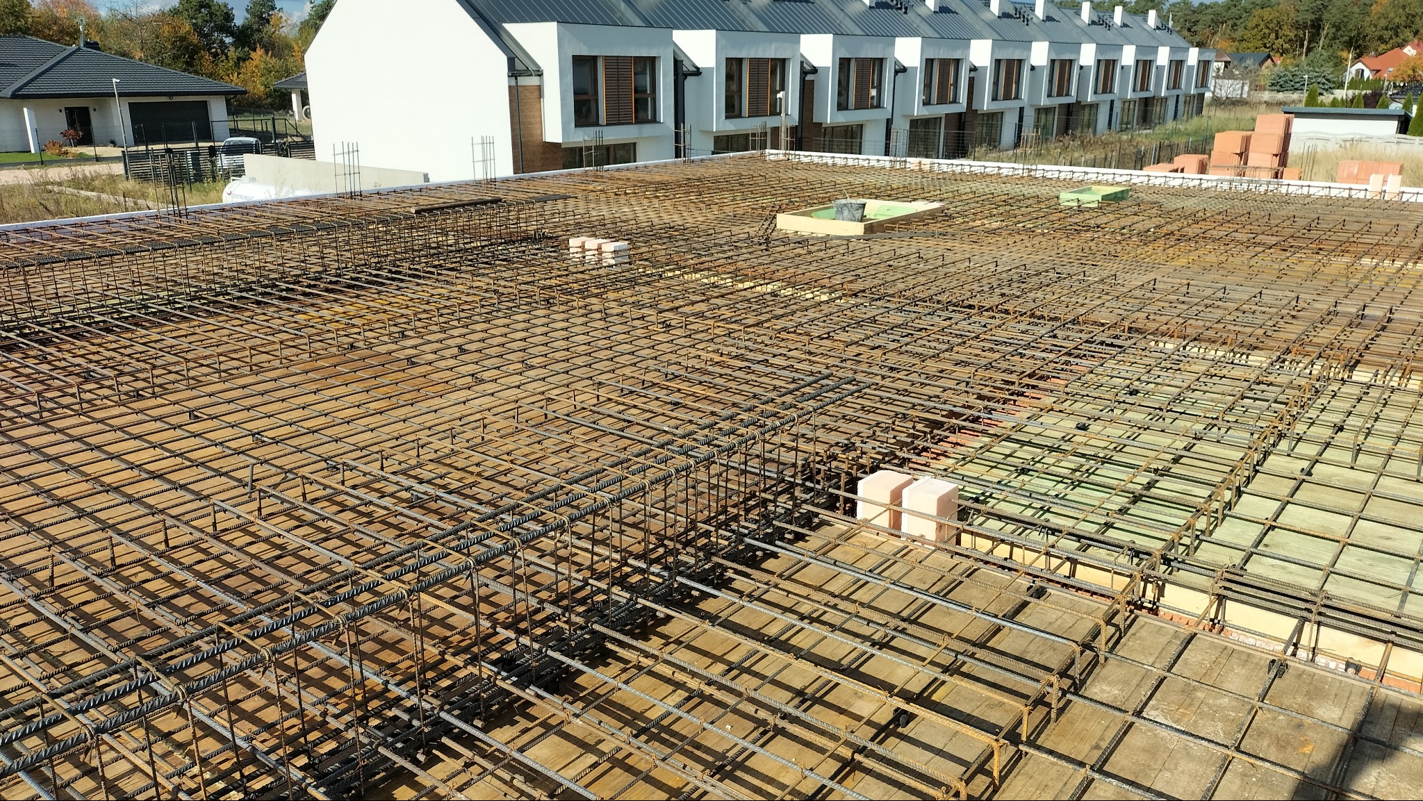 Zbrojenie stropu na budowie domu w Tomaszowie Mazowieckim, widoczne z góry, z ułożonymi bloczkami i deskowaniem. W tle budynki w zabudowie szeregowej.