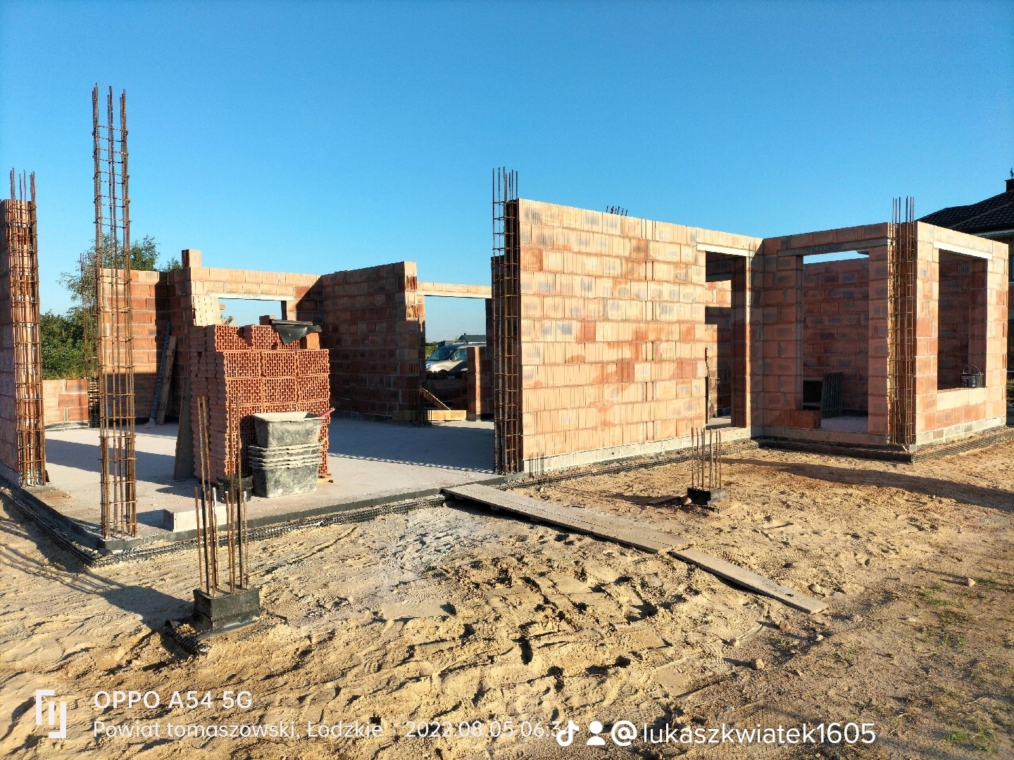 Wznoszenie ścian zewnętrznych z bloczków ceramicznych na fundamencie domu jednorodzinnego, widoczne zbrojenia pionowe i zapas bloczków obok ściany.