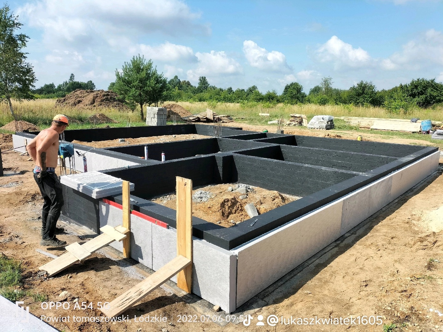 Fundamenty domu jednorodzinnego z izolacją termiczną, widoczny pracownik w kasku i bez koszulki, przygotowujący się do dalszych prac.