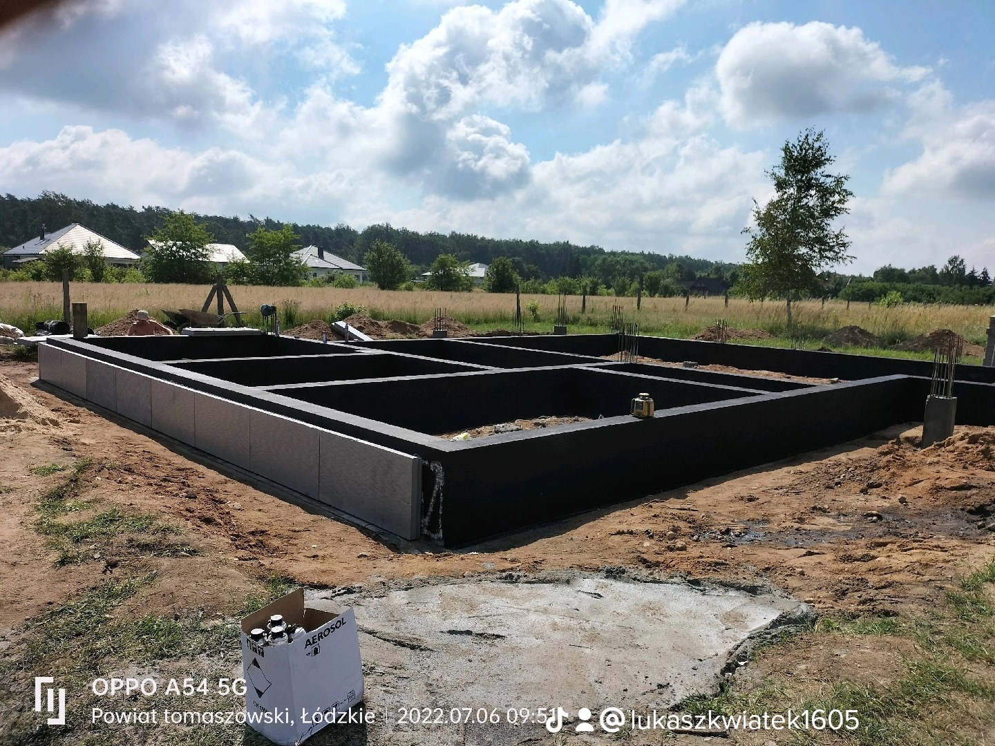 Zabezpieczony fundament domu jednorodzinnego, widoczne szalunki i izolacja termiczna, w tle łąka i zabudowania.