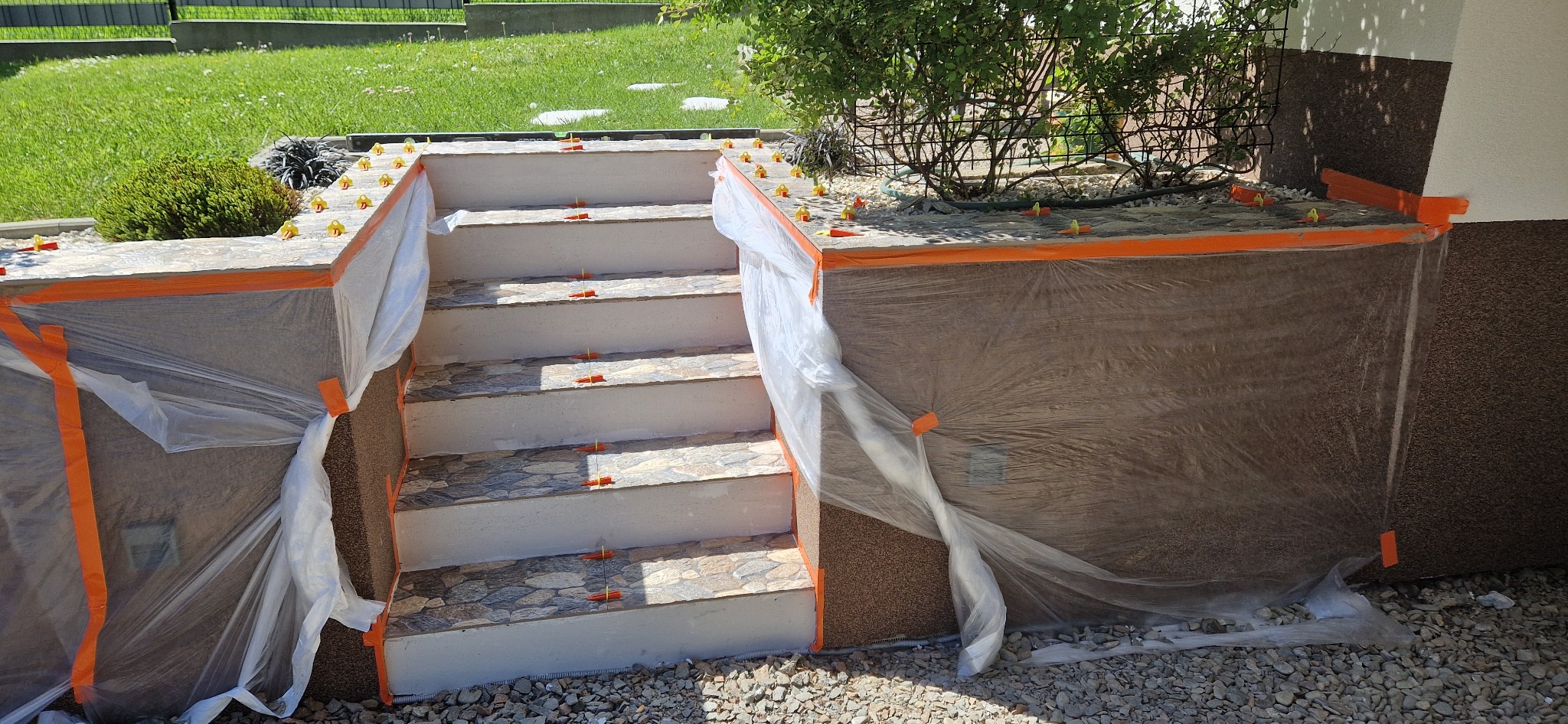 Zewnętrzne schody wejściowe z nową okładziną z płytek, zabezpieczone folią i taśmą malarską podczas prac wykończeniowych.